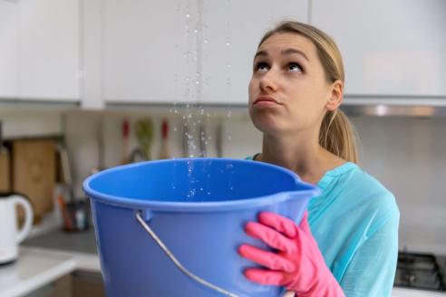 Woman holding bucket to catch water leaking from ceiling
